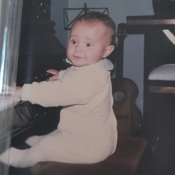 Thiago Melo ainda bebê, ao piano de casa, com o violão ao lado